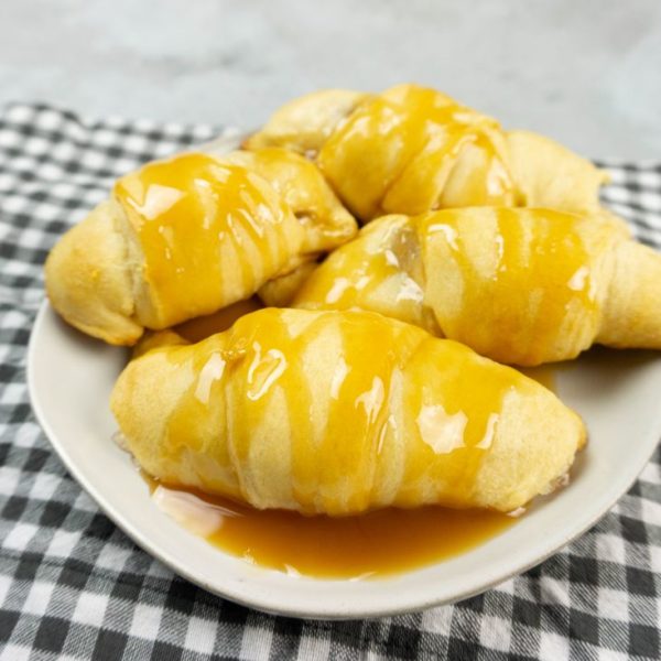 Apple Dumpling Croissants on a white plate with caramel drizzle with white and gray napkin on a concrete backdrop