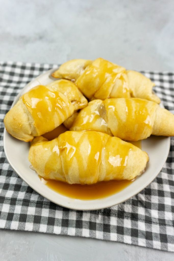 Apple Dumpling Croissants on a white plate with caramel drizzle with white and gray napkin on a concrete backdrop