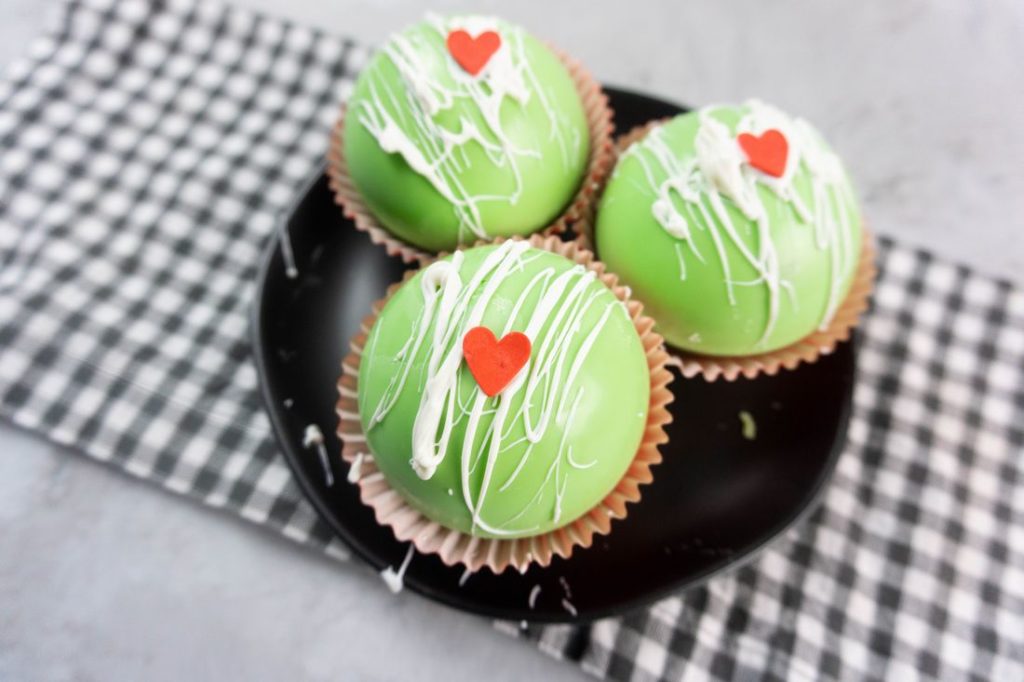 Grinch Hot Chocolate Bombs on a black plate on a grey plaid napkin with a concrete backdrop