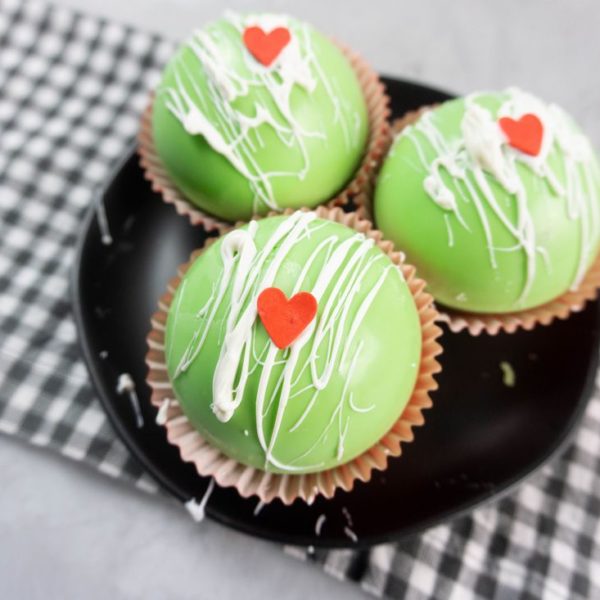 Grinch Hot Chocolate Bombs on a black plate on a grey plaid napkin with a concrete backdrop