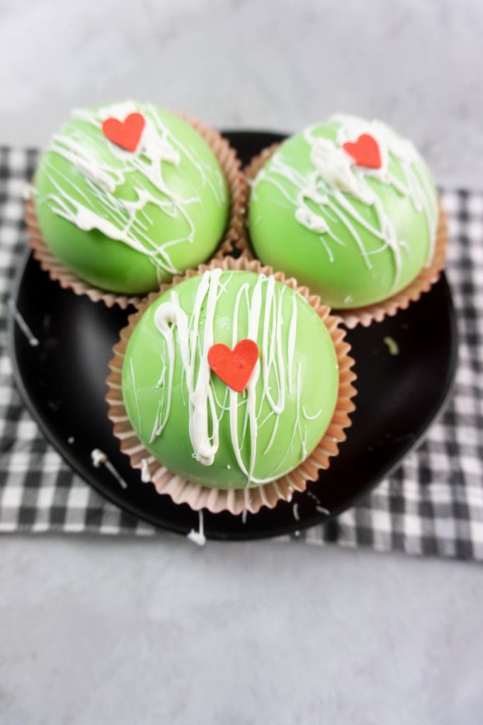 Grinch Hot Chocolate Bombs on a black plate on a grey plaid napkin with a concrete backdrop