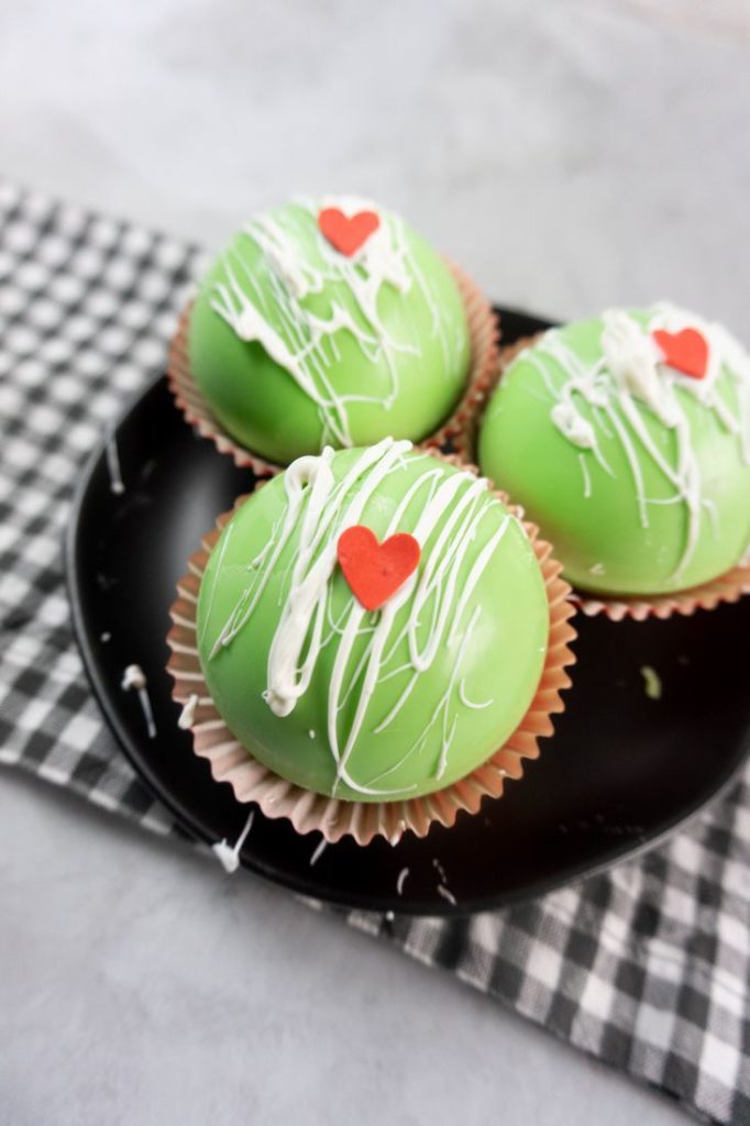 Grinch Hot Chocolate Bombs on a black plate on a grey plaid napkin with a concrete backdrop