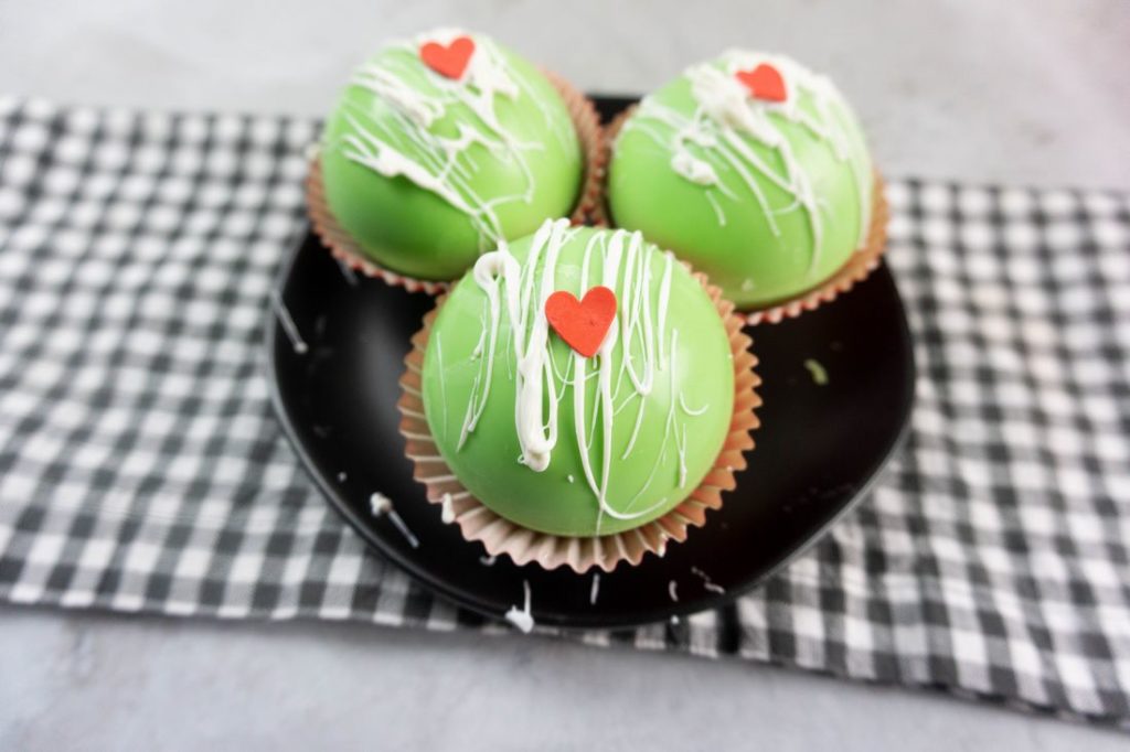 Grinch Hot Chocolate Bombs on a black plate on a grey plaid napkin with a concrete backdrop