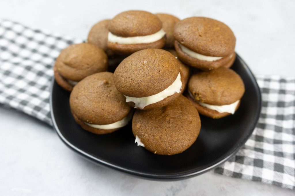 Pumpkin Whoopie Pies on a black plate with gray and white plaid napkin on a concrete backdrop