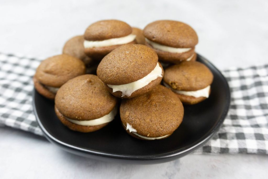 Pumpkin Whoopie Pies on a black plate with gray and white plaid napkin on a concrete backdrop
