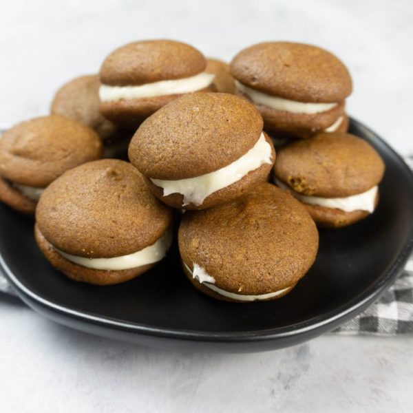 Pumpkin Whoopie Pies on a black plate with gray and white plaid napkin on a concrete backdrop