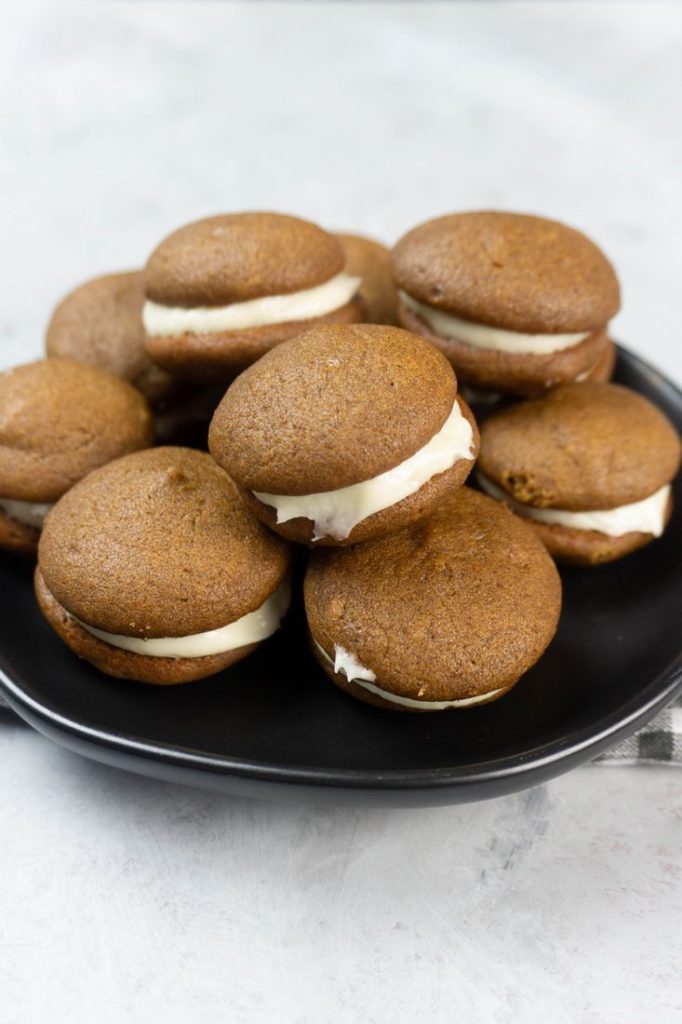 Pumpkin Whoopie Pies on a black plate with gray and white plaid napkin on a concrete backdrop