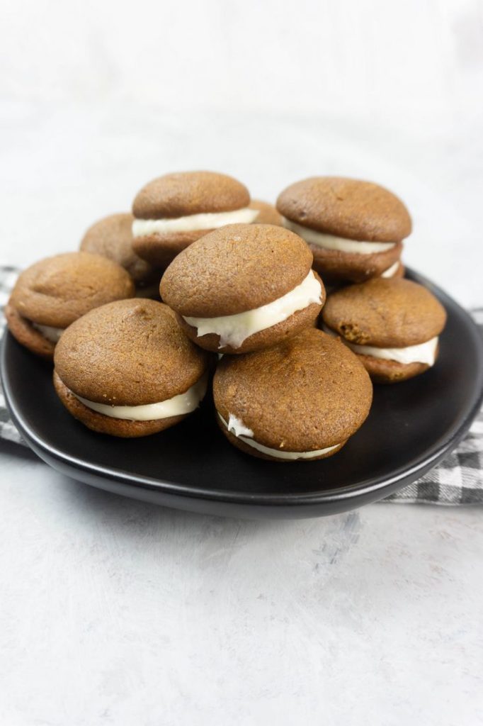 Pumpkin Whoopie Pies on a black plate with gray and white plaid napkin on a concrete backdrop