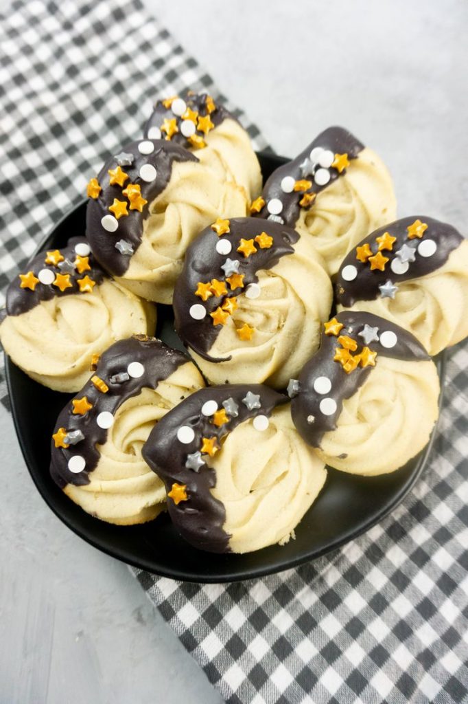 New Year's Eve Dipped Butter Cookies on a black plate with gray plaid napkin and concrete backdrop