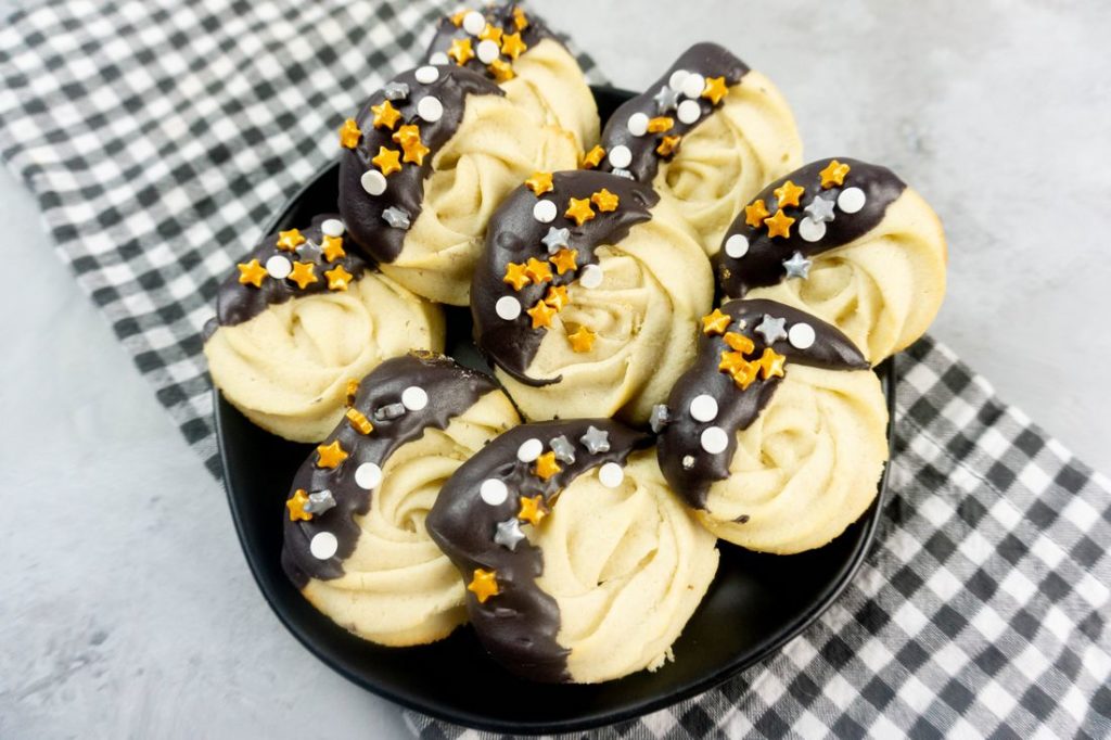 New Year's Eve Dipped Butter Cookies on a black plate with gray plaid napkin and concrete backdrop