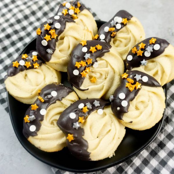 New Year's Eve Dipped Butter Cookies on a black plate with gray plaid napkin and concrete backdrop