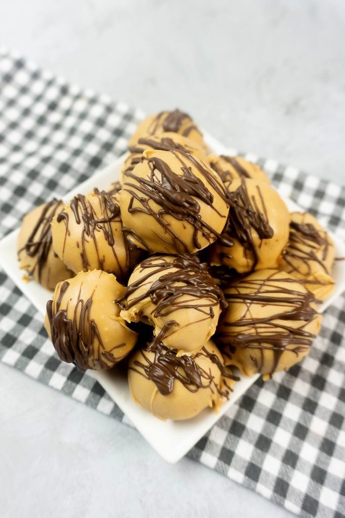 Peanut Butter Truffles drizzled with milk chocolate on a white plate with a gray plaid napkin and concrete back drop