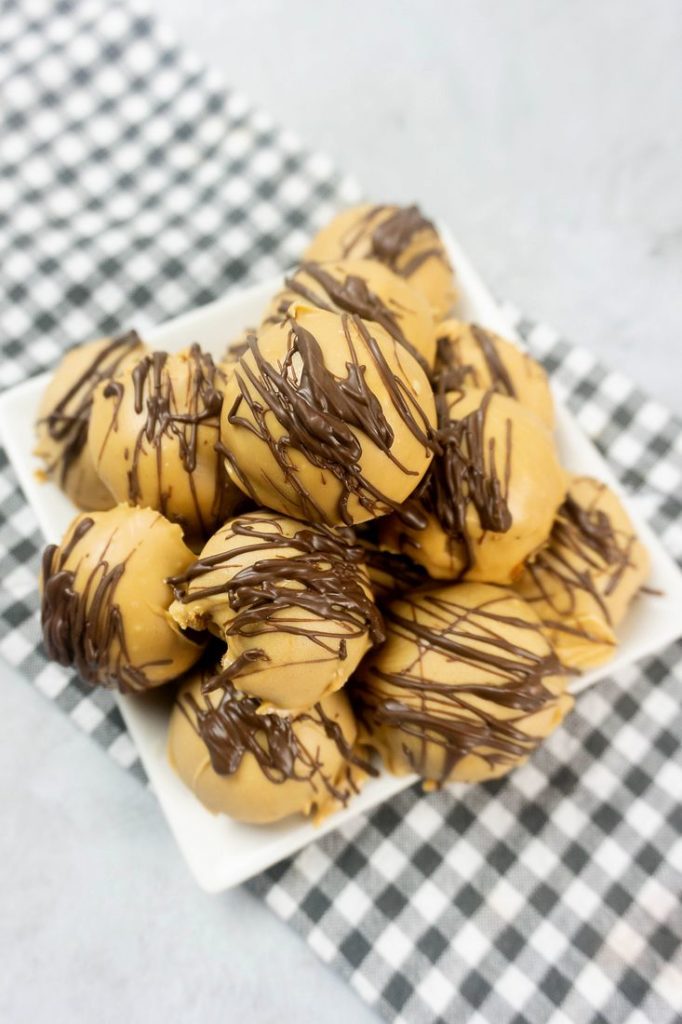 Peanut Butter Truffles drizzled with milk chocolate on a white plate with a gray plaid napkin and concrete back drop