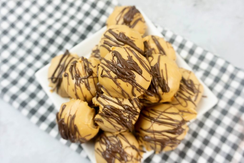 Peanut Butter Truffles drizzled with milk chocolate on a white plate with a gray plaid napkin and concrete back drop