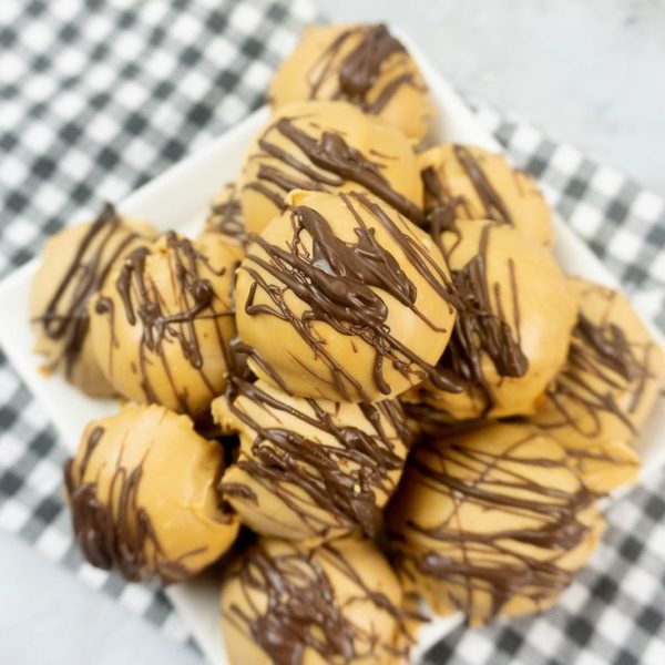 Peanut Butter Truffles drizzled with milk chocolate on a white plate with a gray plaid napkin and concrete back drop