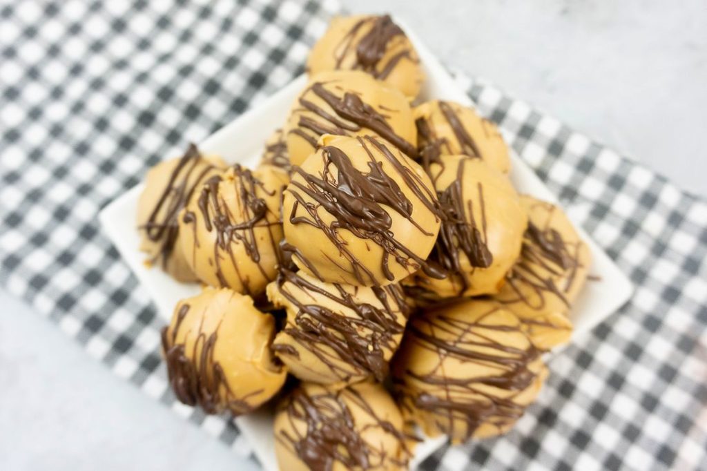 Peanut Butter Truffles drizzled with milk chocolate on a white plate with a gray plaid napkin and concrete back drop