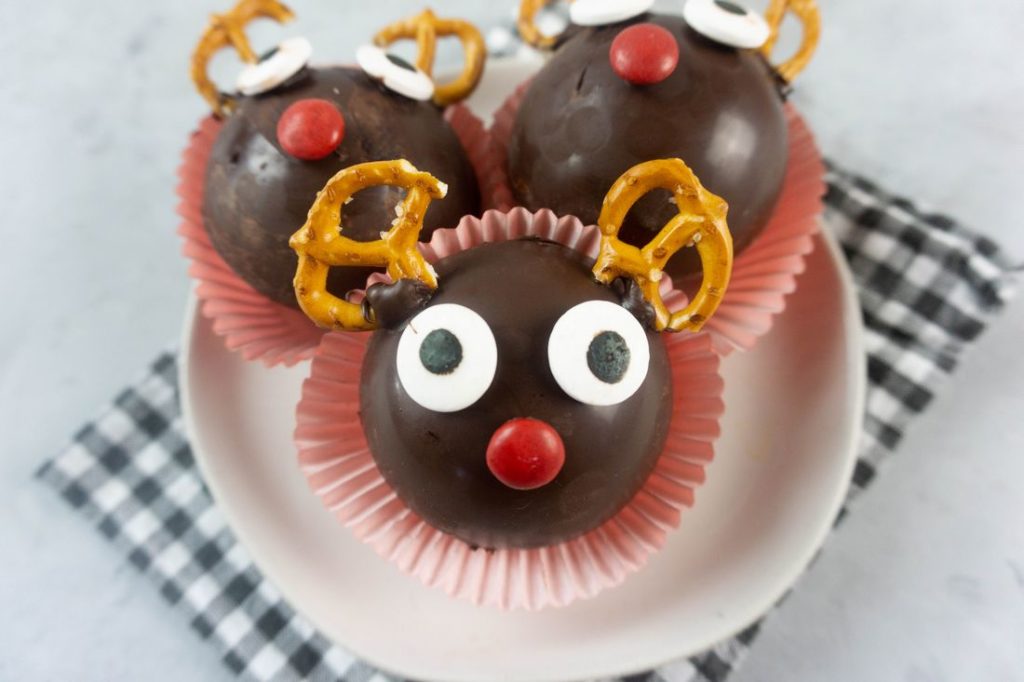 Rudolph Hot Chocolate Bombs on a white plate with gray plaid napkin and concrete backdrop