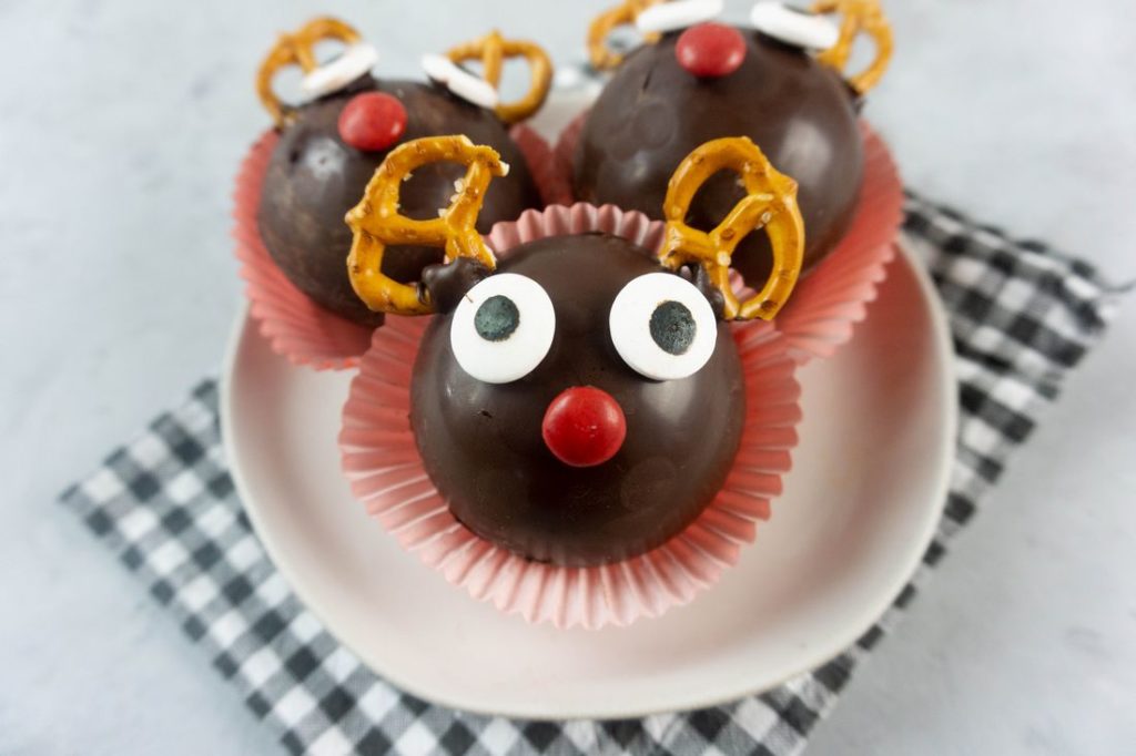 Rudolph Hot Chocolate Bombs on a white plate with gray plaid napkin and concrete backdrop