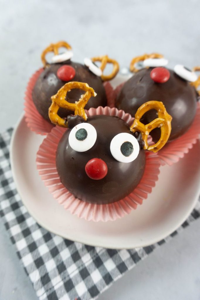 Rudolph Hot Chocolate Bombs on a white plate with gray plaid napkin and concrete backdrop