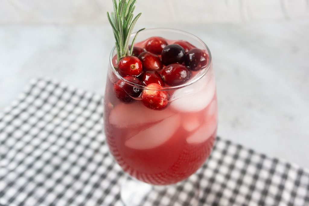 Rudolph Spritzer with cranberries and fresh rosemary in a glass on a gray plaid napkin and concrete backdrop