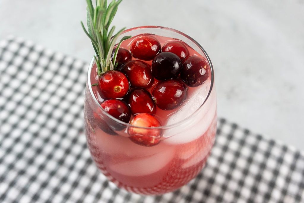 Rudolph Spritzer with cranberries and fresh rosemary in a glass on a gray plaid napkin and concrete backdrop