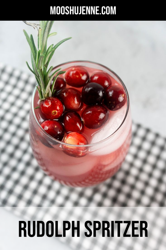 Rudolph Spritzer with cranberries and fresh rosemary in a glass on a gray plaid napkin and concrete backdrop