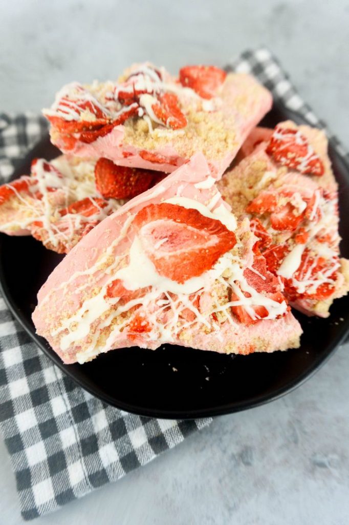 Strawberry Shortcake Bark on a black plate with grey and white plaid napkin on a concrete backdrop