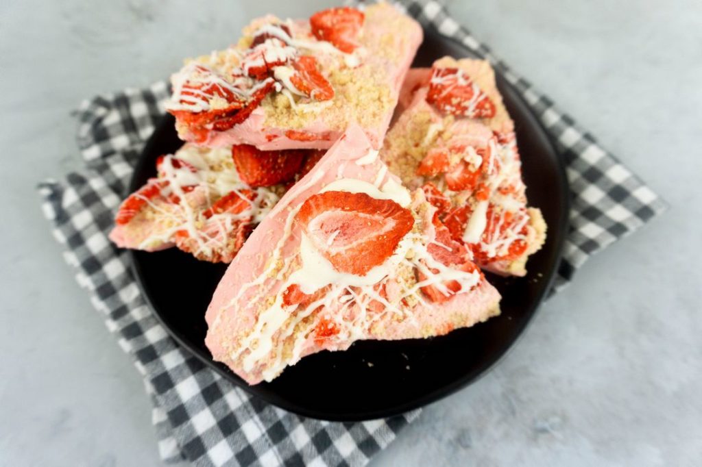 Strawberry Shortcake Bark on a black plate with grey and white plaid napkin on a concrete backdrop