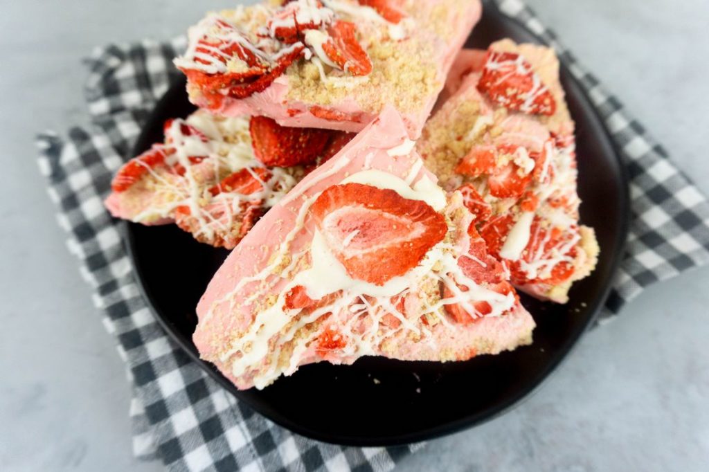 Strawberry Shortcake Bark on a black plate with grey and white plaid napkin on a concrete backdrop