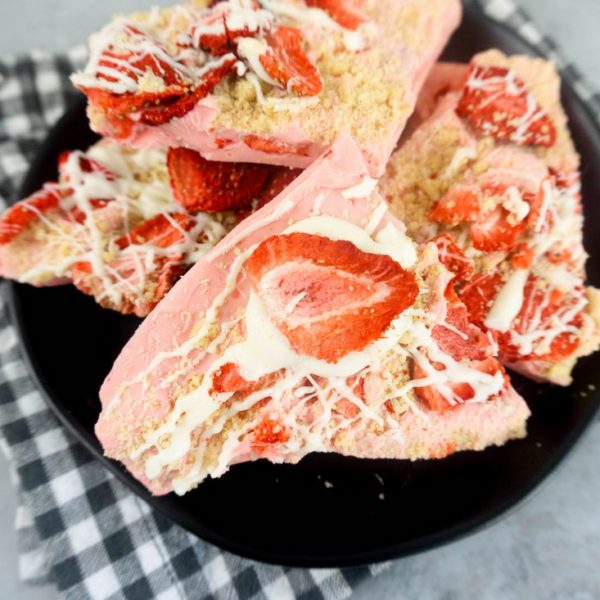 Strawberry Shortcake Bark on a black plate with grey and white plaid napkin on a concrete backdrop