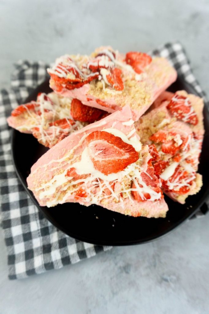 Strawberry Shortcake Bark on a black plate with grey and white plaid napkin on a concrete backdrop