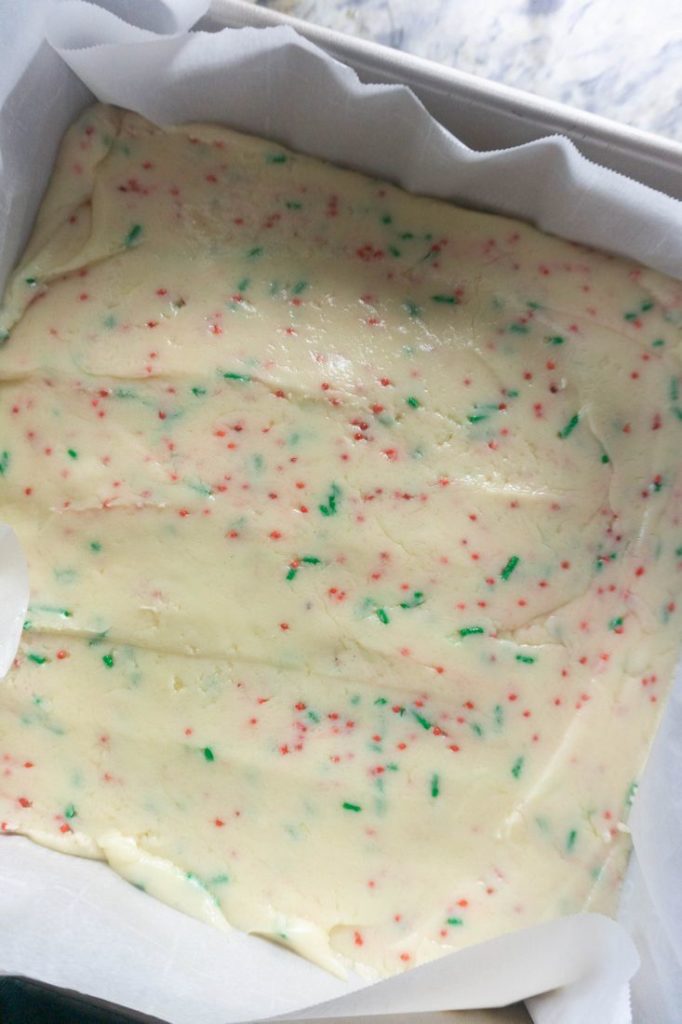 Sugar cookie fudge in a pan lined with parchment paper.