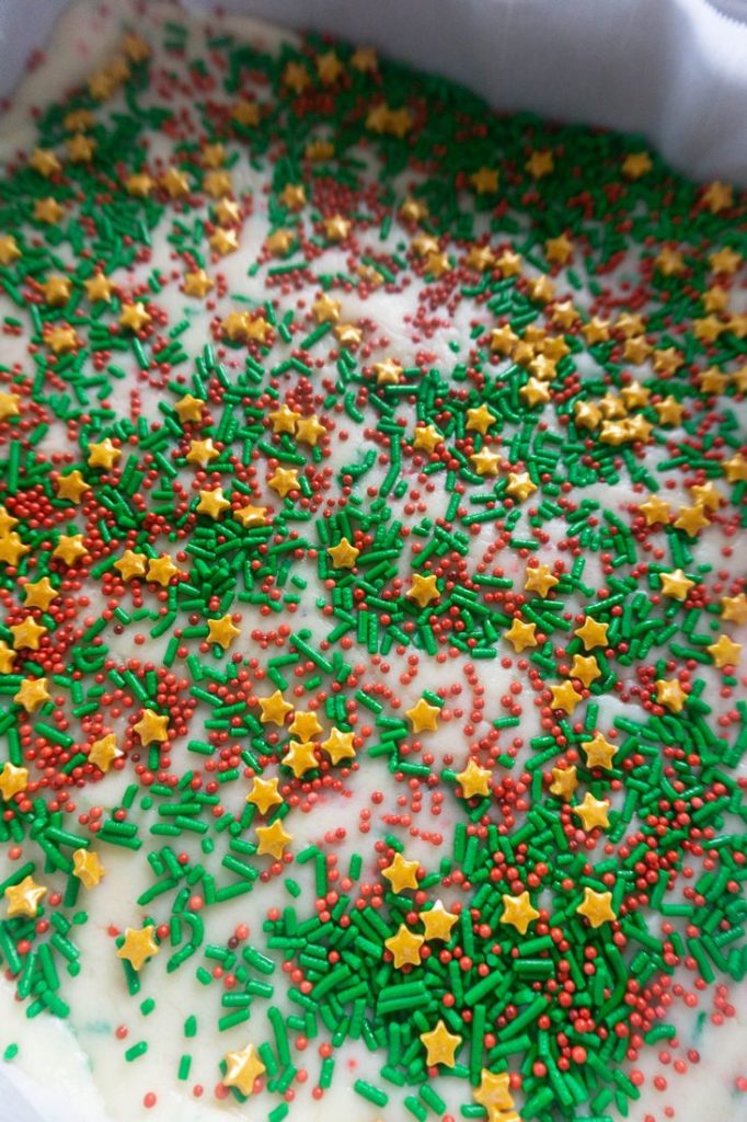 Sugar cookie fudge in a pan lined with parchment paper topped with crazy amounts of sprinkles