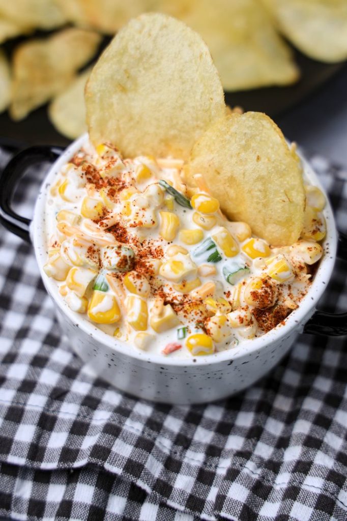 Southwestern Corn Dip in a white and black speckled bowl with a gray plaid napkin on a concrete backdrop