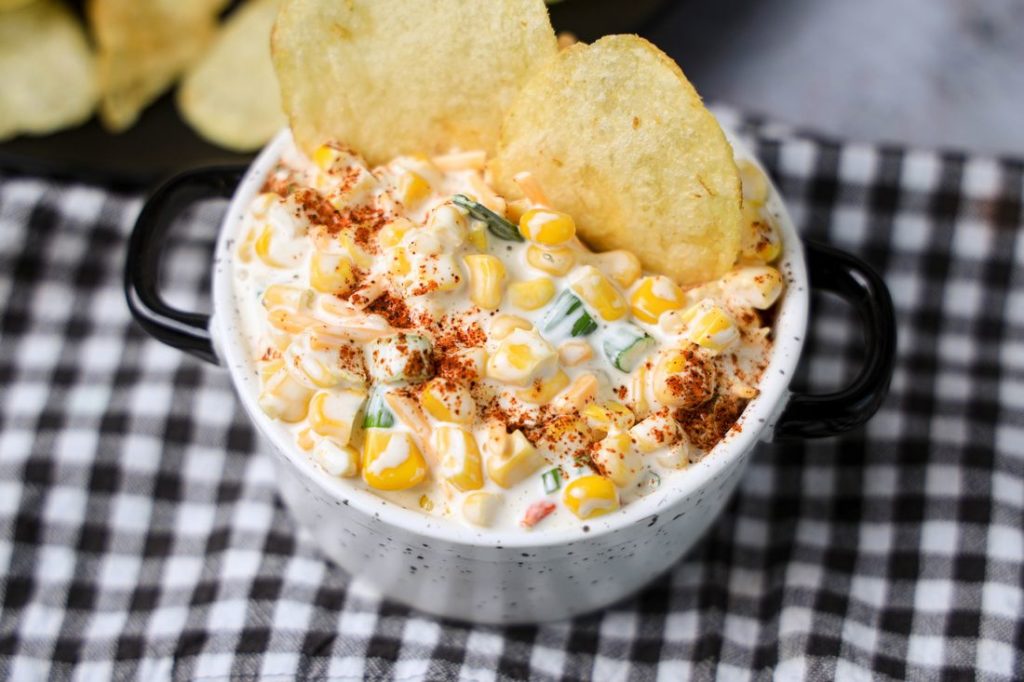 Southwestern Corn Dip in a white and black speckled bowl with a gray plaid napkin on a concrete backdrop