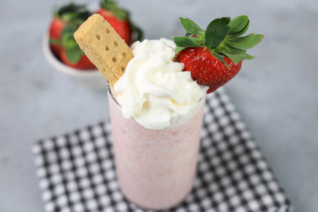 Strawberry Shortcake Shake in a glass with strawberry on top on a gray plaid napkin on a concrete backdrop