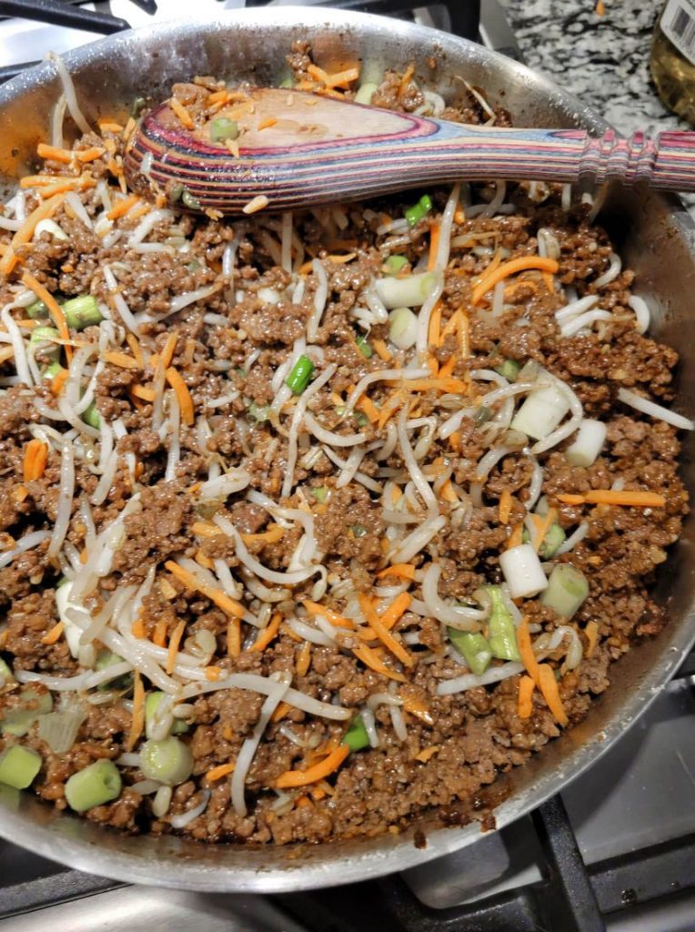Ground beef , spring onions, carrots, and mung bean sprouts in a frying pan