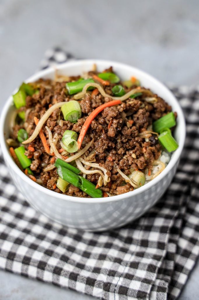 Beef in a bowl with mung bean sprouts, carrots, and spring onions. On a gray plaid napkin with concrete backdrop