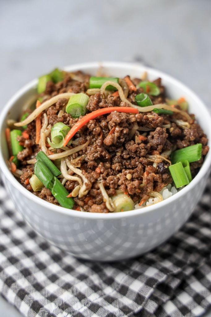 Beef in a bowl with mung bean sprouts, carrots, and spring onions. On a gray plaid napkin with concrete backdrop