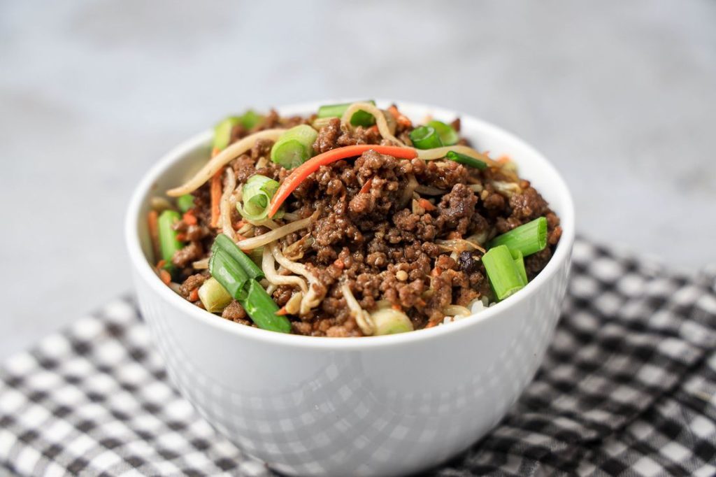 Beef in a bowl with mung bean sprouts, carrots, and spring onions. On a gray plaid napkin with concrete backdrop