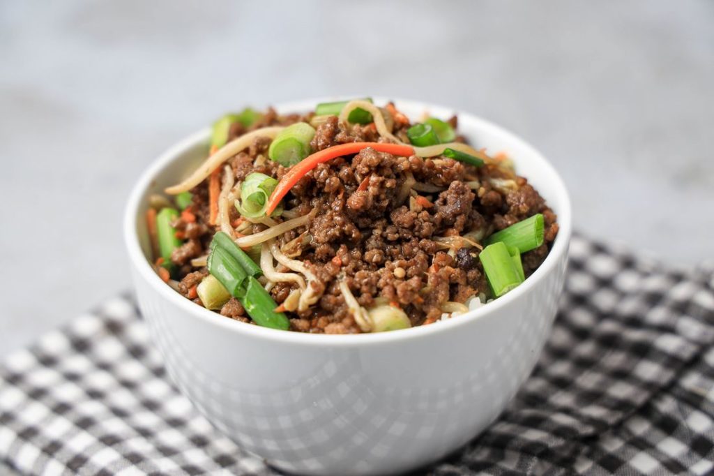 Beef in a bowl with mung bean sprouts, carrots, and spring onions. On a gray plaid napkin with concrete backdrop