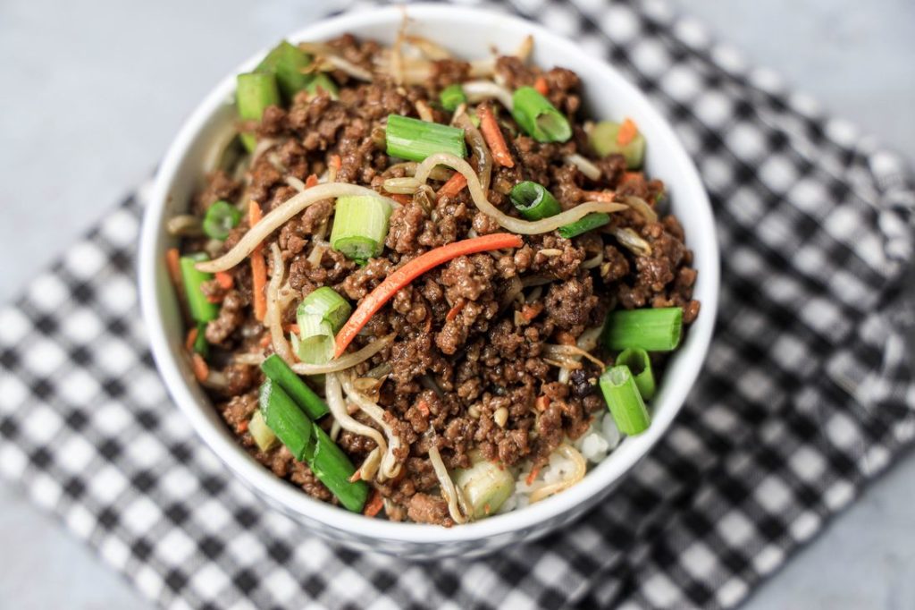 Beef in a bowl with mung bean sprouts, carrots, and spring onions. On a gray plaid napkin with concrete backdrop