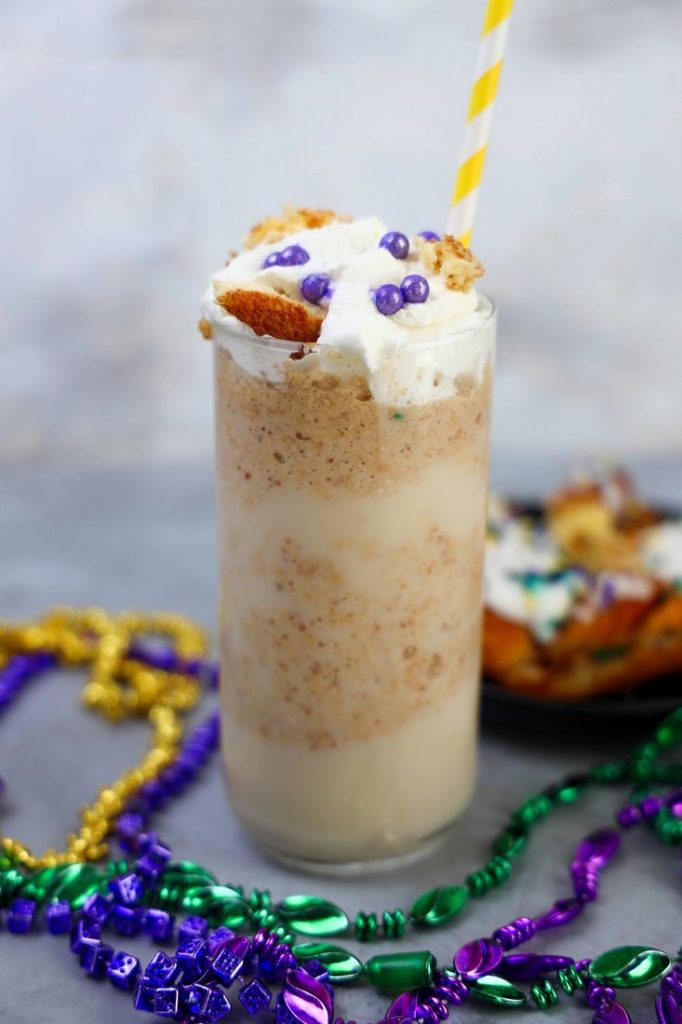 King Cake Frappuccino in a tall glass topped with whipped topping, purple pearl candies, and a yellow straw.