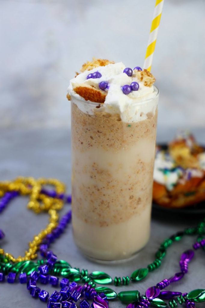 King Cake Frappuccino in a tall glass topped with whipped topping, purple pearl candies, and a yellow straw.