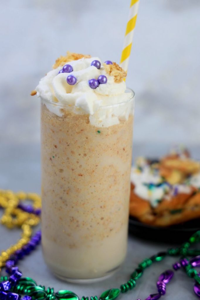 King Cake Frappuccino in a tall glass topped with whipped topping, purple pearl candies, and a yellow straw.