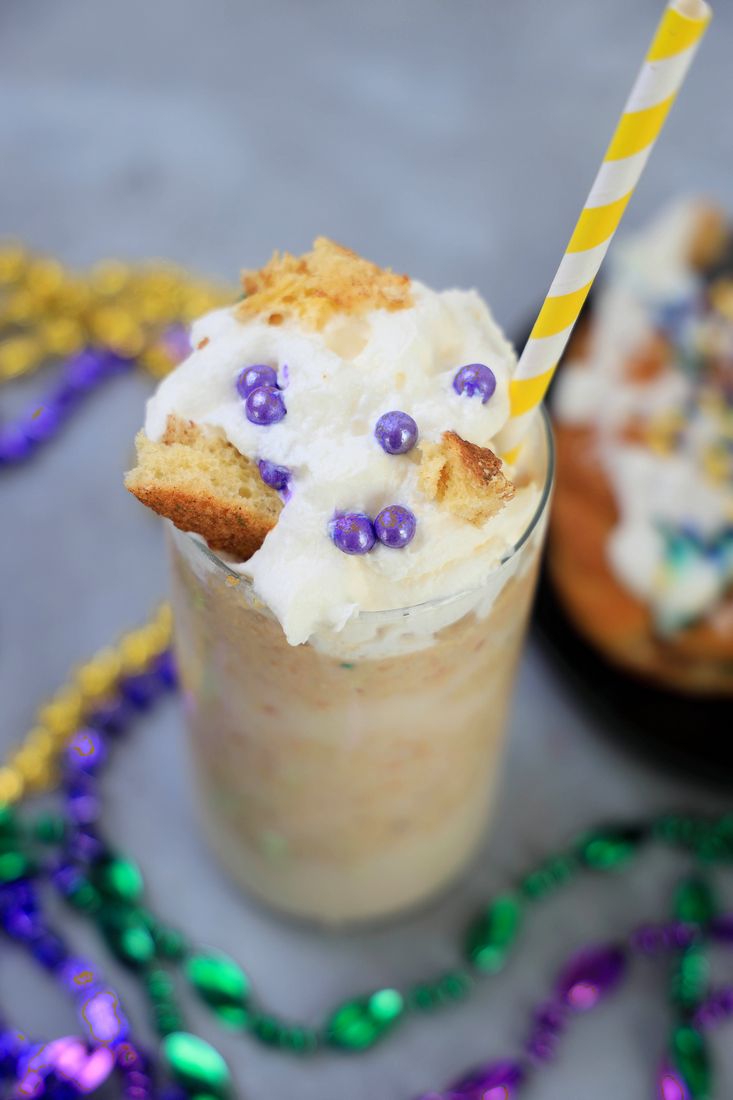 King Cake Frappuccino in a tall glass topped with whipped topping, purple pearl candies, and a yellow straw.
