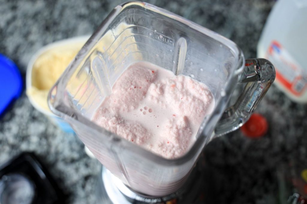 Strawberry Shortcake Shake in a glass with strawberry on top on a gray plaid napkin on a concrete backdrop