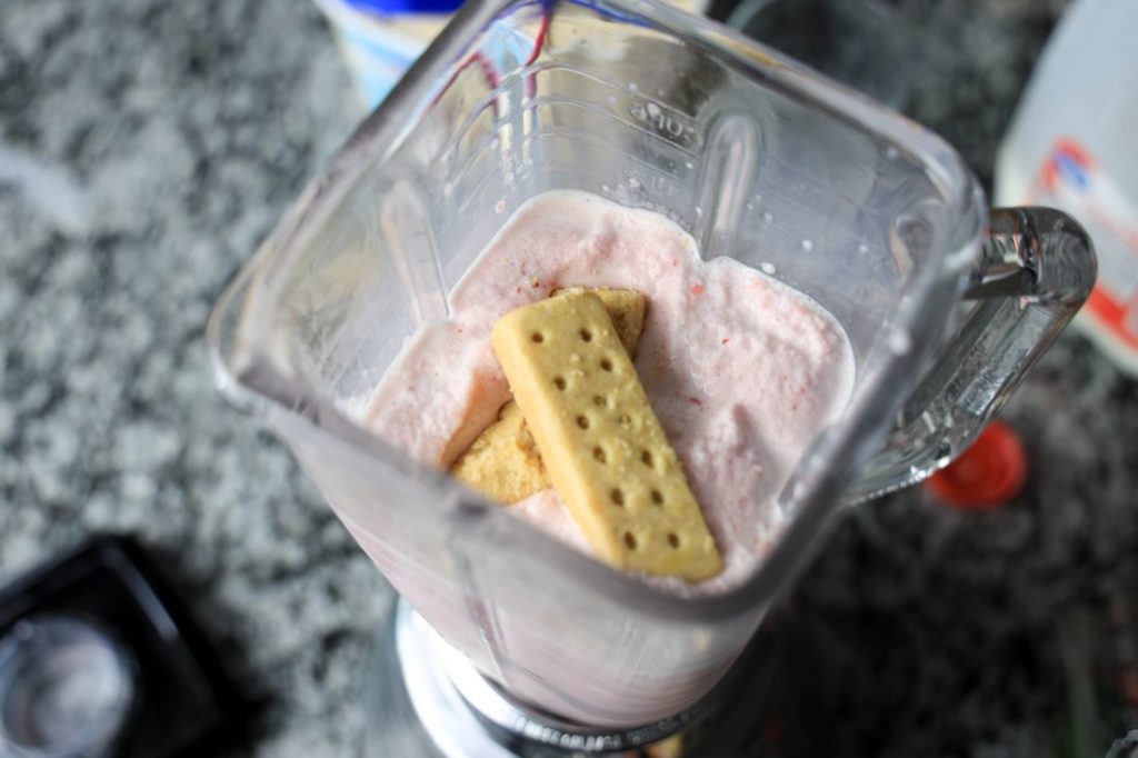 Strawberry Shortcake Shake in a glass with strawberry on top on a gray plaid napkin on a concrete backdrop