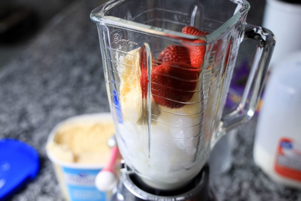 Strawberry Shortcake Shake in a glass with strawberry on top on a gray plaid napkin on a concrete backdrop