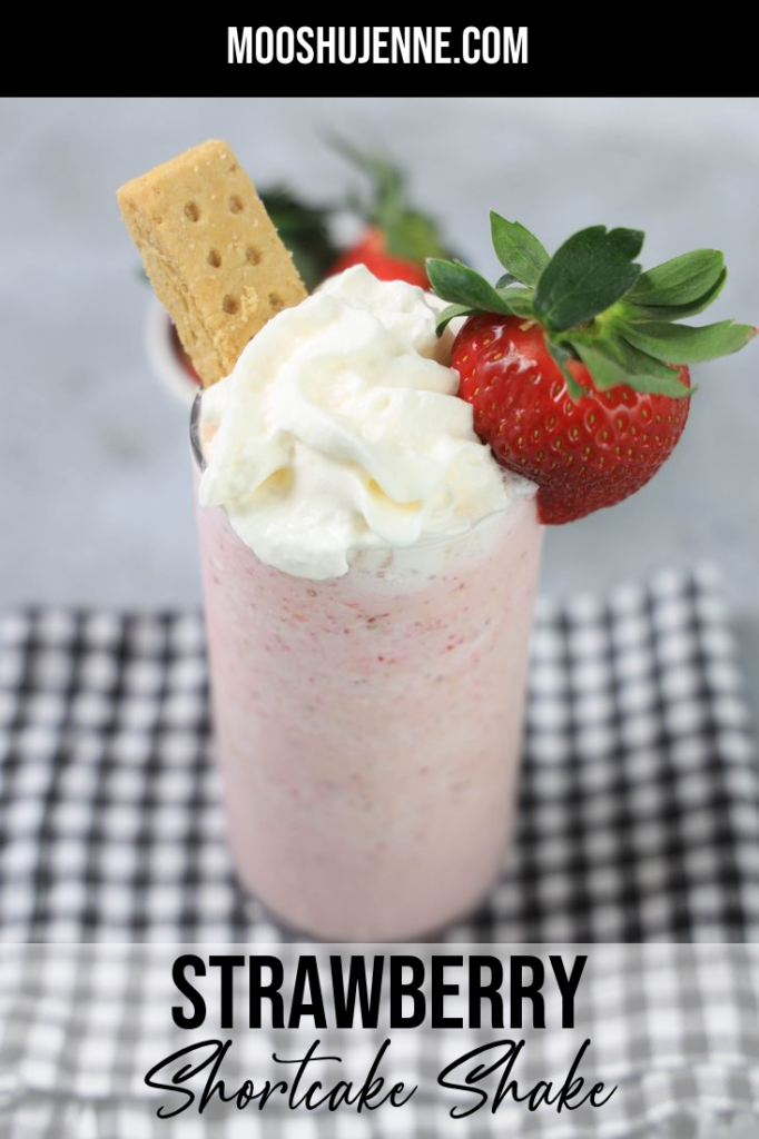 Strawberry Shortcake Shake in a glass with strawberry on top on a gray plaid napkin on a concrete backdrop